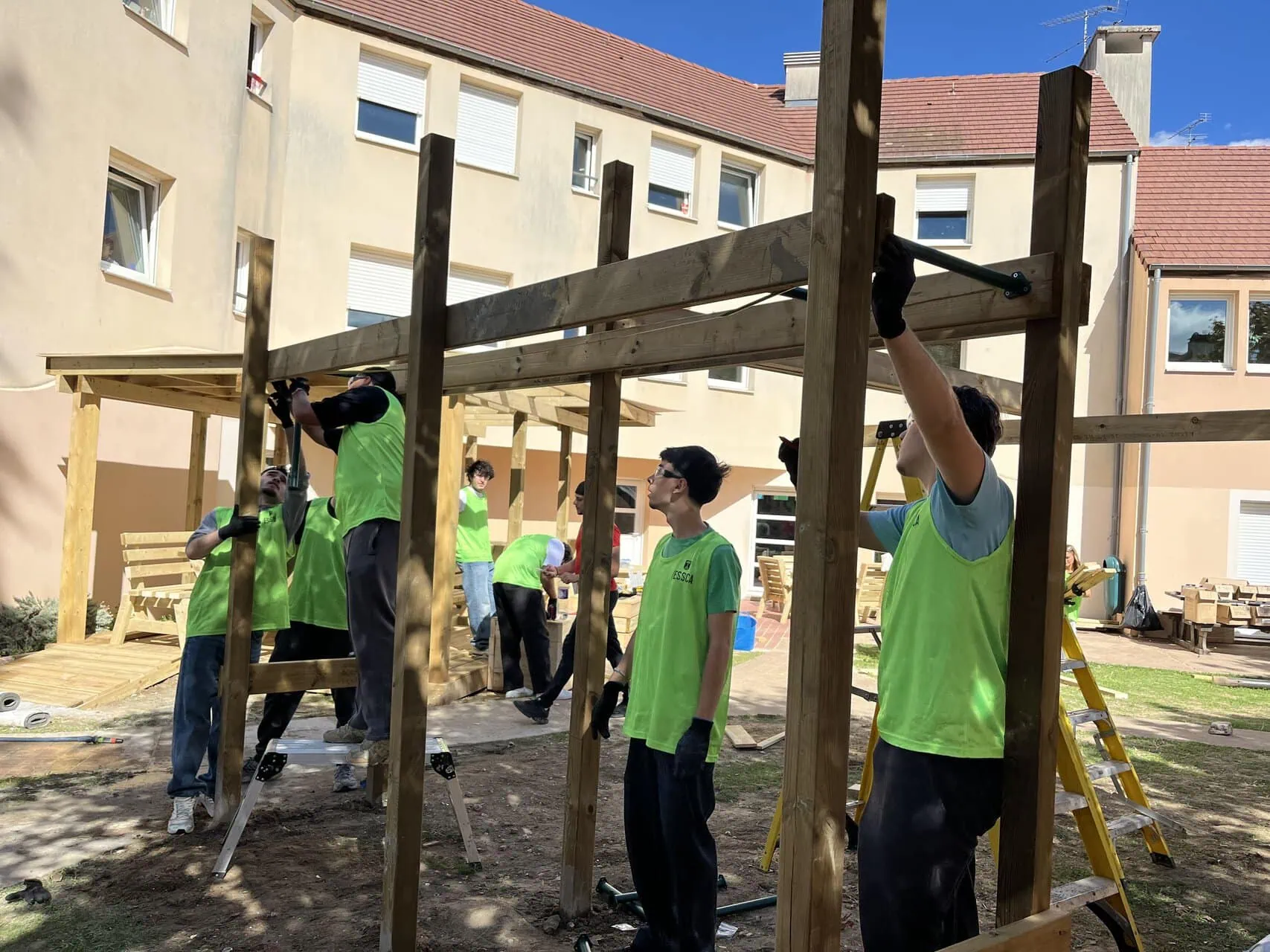 Chantier montage ossature bois en cour : équipe installe poteaux et poutres pour abri.