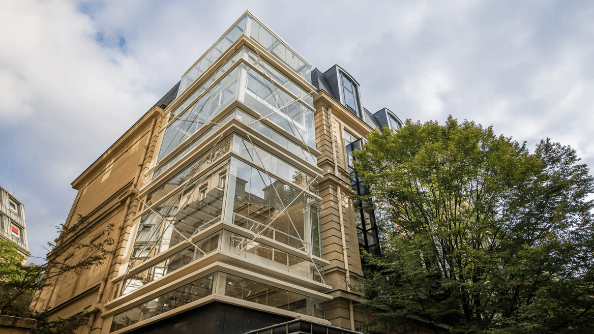Bâtiment coin contemporain en verre et pierre, escalier vitré moderne contre façade historique.