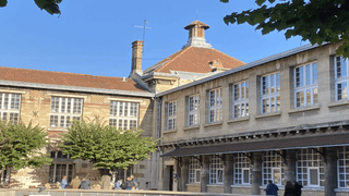 Cour intérieure dun bâtiment historique en pierre et brique, toit en tuiles, arbres et bancs.