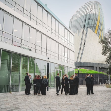 Cour urbaine de lécole Vatel avec tour moderne et groupes de personnes.