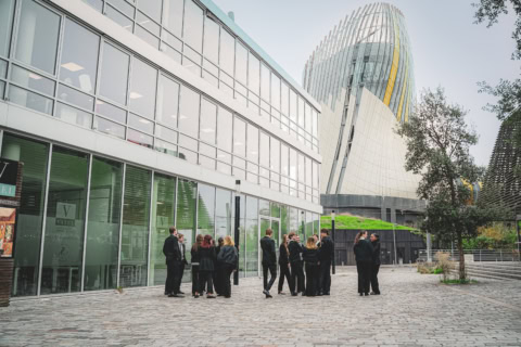 Cour urbaine de lécole Vatel avec tour moderne et groupes de personnes.