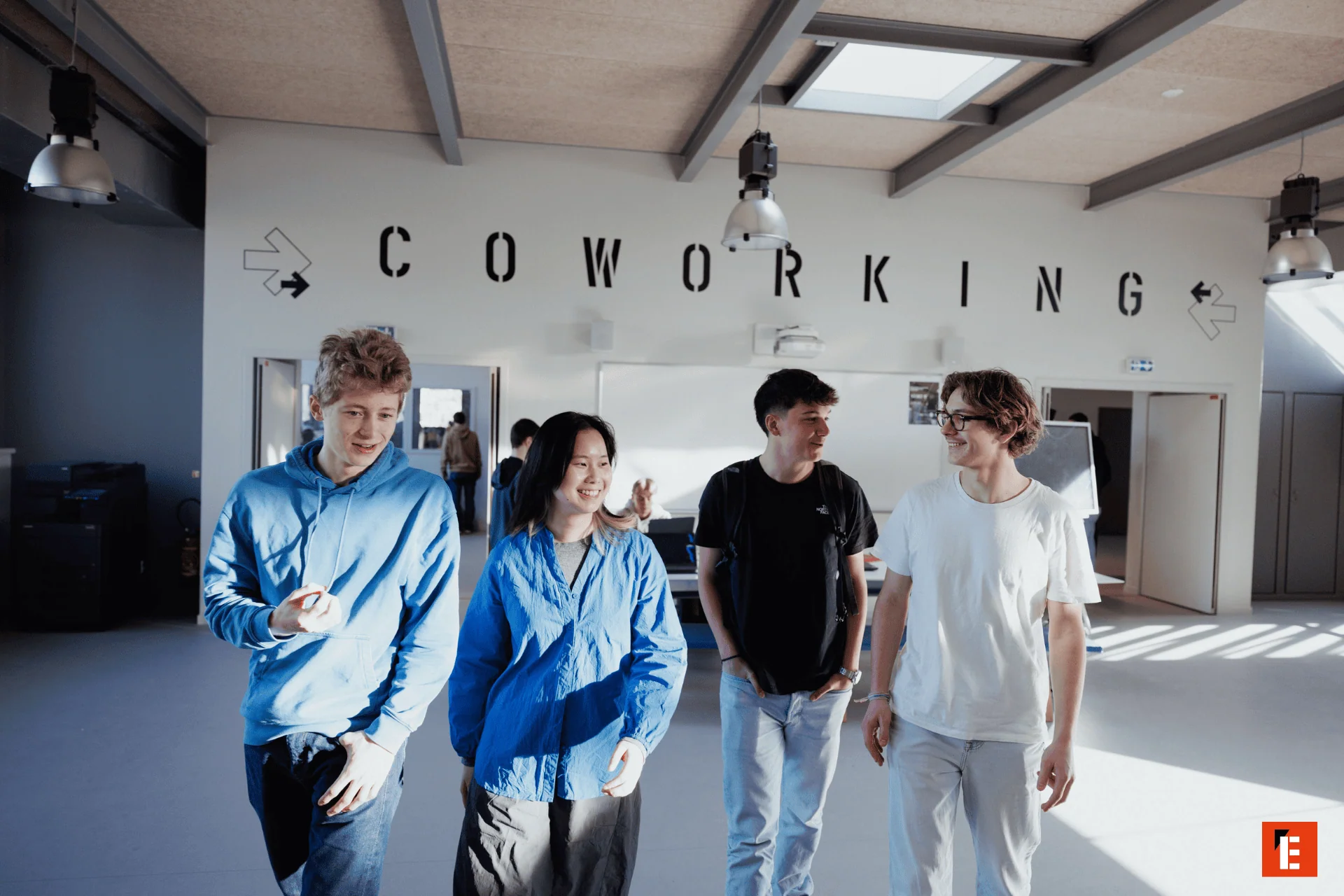 Espace coworking lumineux avec jeunes professionnels marchant et travaillant en espace ouvert.