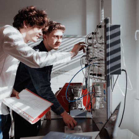 Deux étudiants au laboratoire testent un banc dessai électronique avec câbles et instruments.