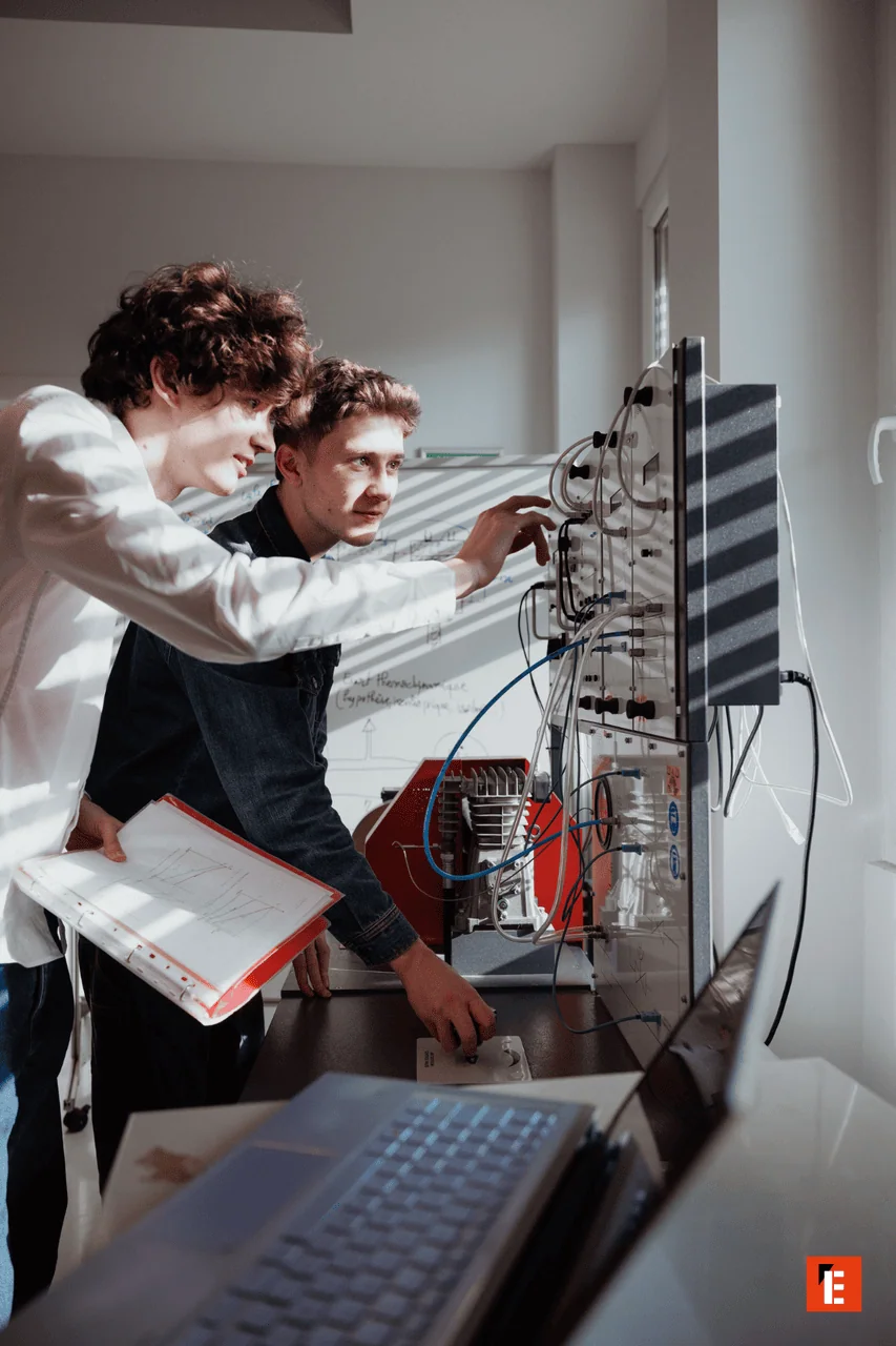 Deux étudiants au laboratoire testent un banc dessai électronique avec câbles et instruments.