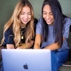 Deux jeunes femmes souriantes utilisant un MacBook, ordinateur portable, travail collaboratif.