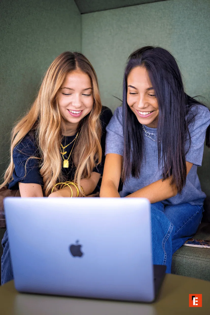 Deux jeunes femmes souriantes utilisant un MacBook, ordinateur portable, travail collaboratif.