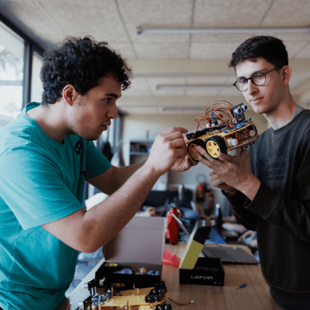 Deux personnes assemblent robot mobile dans atelier de robotique, électronique, prototypage.