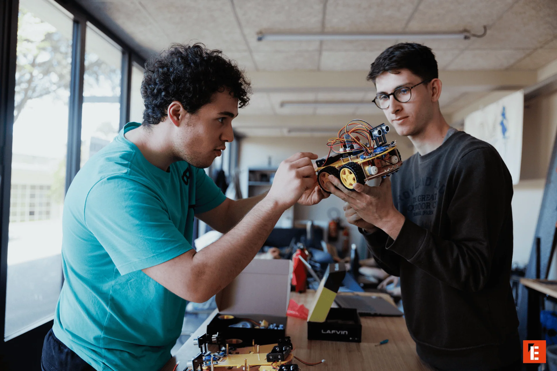 Deux personnes assemblent robot mobile dans atelier de robotique, électronique, prototypage.