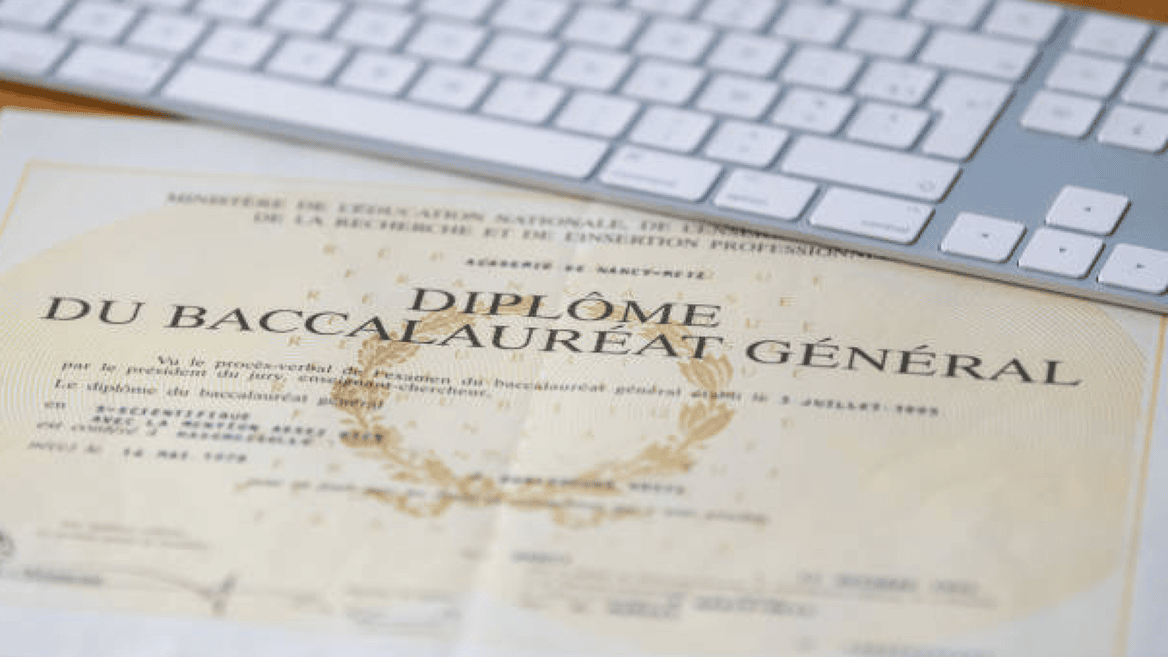 Diplôme du baccalauréat sur bureau avec clavier blanc, laurier doré et pli marqué.