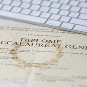 Diplôme du baccalauréat sur bureau avec clavier blanc, laurier doré et pli marqué.
