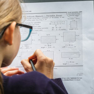Élève concentré en maths écrivant au crayon sur une feuille de mesures.