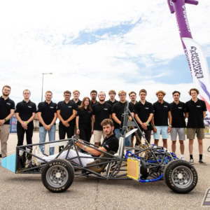 Équipe étudiante présentant voiture prototype monoplace de course légère.