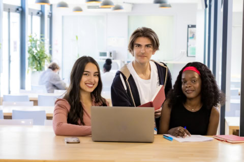 Étudiants en collaboration sur ordinateur portable dans espace détude lumineux et moderne.