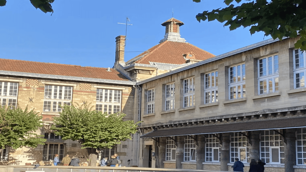 Cour intérieure dun bâtiment historique en pierre et brique, toit en tuiles, arbres et bancs.
