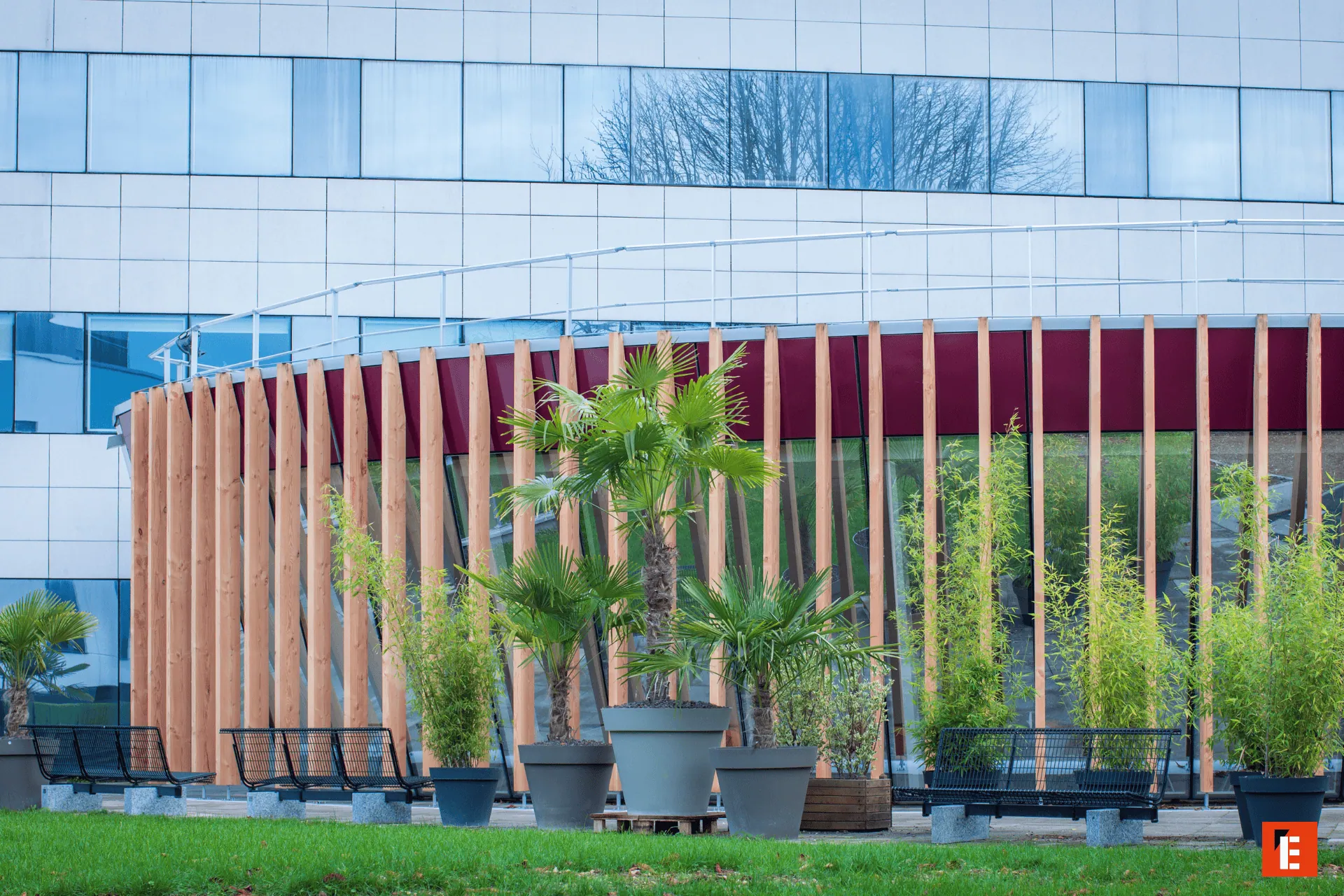 Façade urbaine moderne avec terrasse végétalisée, bancs, lames de bois et fenêtres.