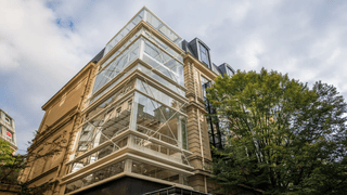 Bâtiment coin contemporain en verre et pierre, escalier vitré moderne contre façade historique.