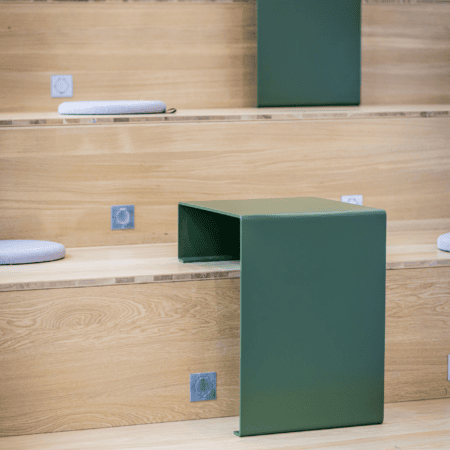 Gradins en chêne minimalistes avec tables vertes, coussins gris et prises intégrées.