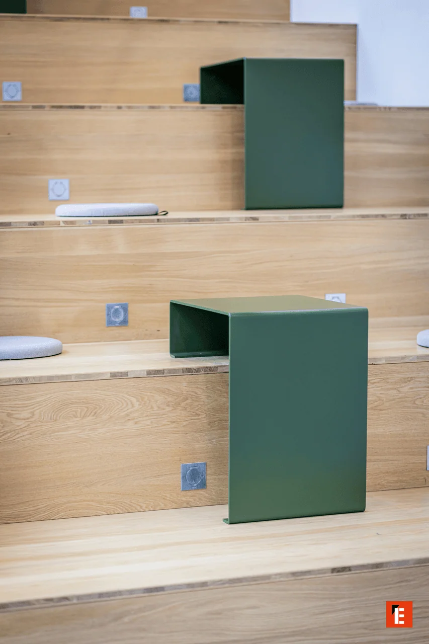 Gradins en chêne minimalistes avec tables vertes, coussins gris et prises intégrées.