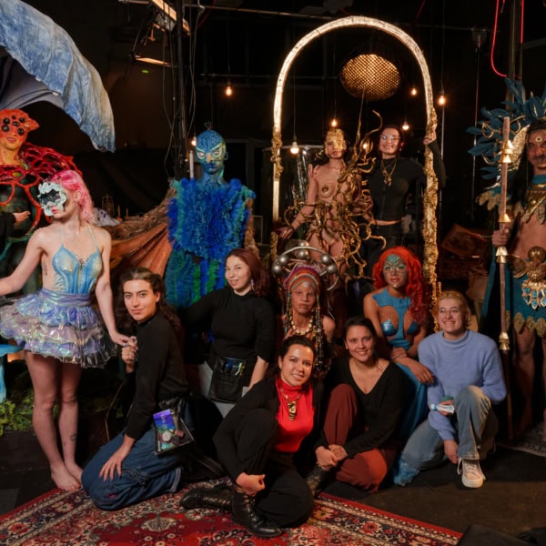 Groupe en coulisses avec costumes théâtraux, maquillage, sculptures et artisans sur scène.
