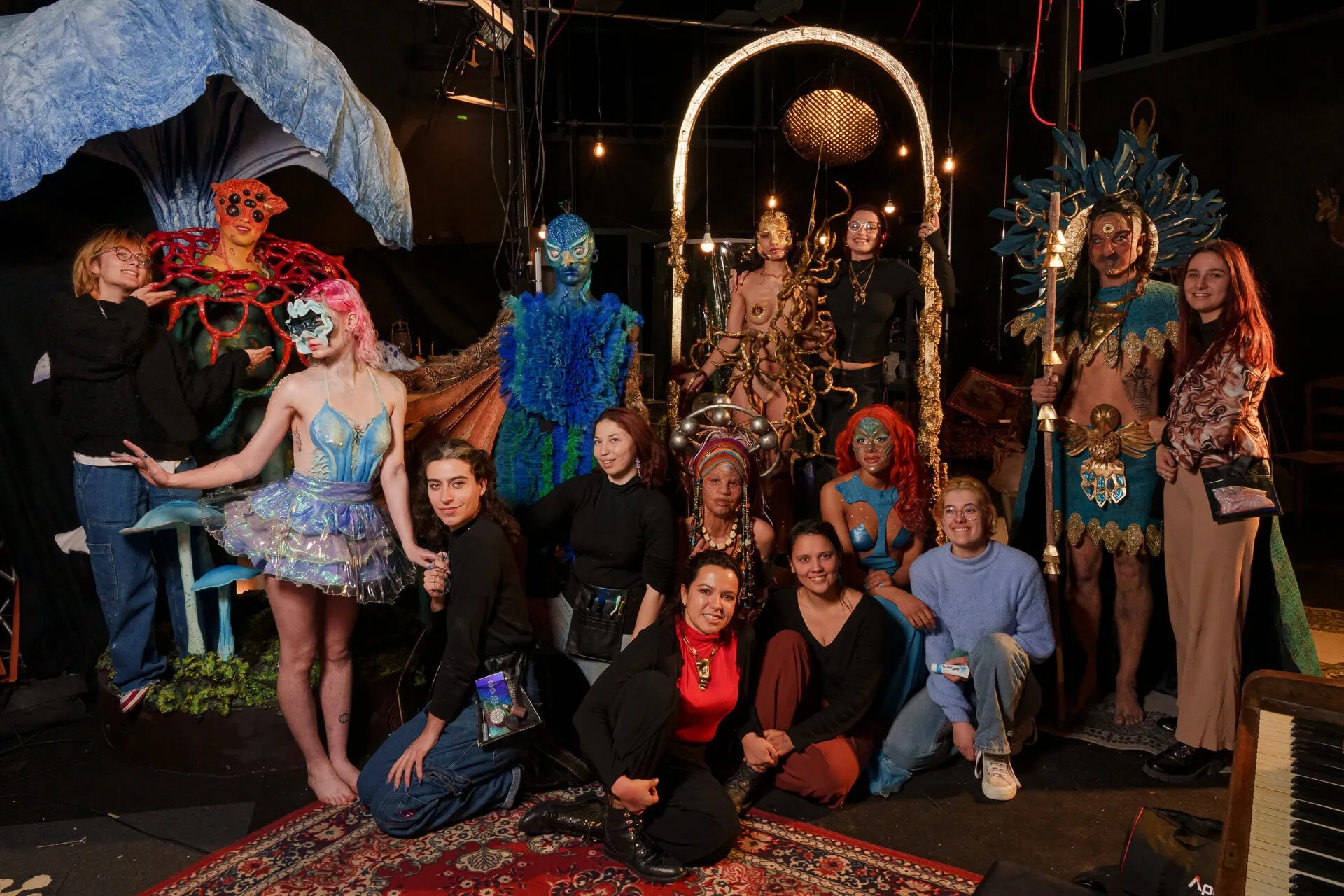Groupe en coulisses avec costumes théâtraux, maquillage, sculptures et artisans sur scène.