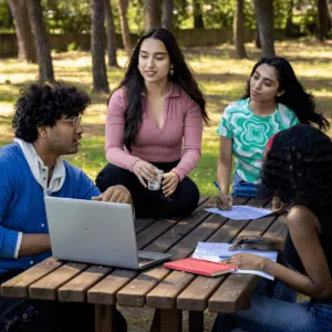Groupe détudiants travaillant en plein air autour dune table de pique-nique avec un ordinateur.