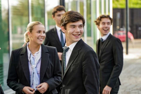 Groupe de jeunes souriants en costumes sur campus urbain, photo spontanée authentique.