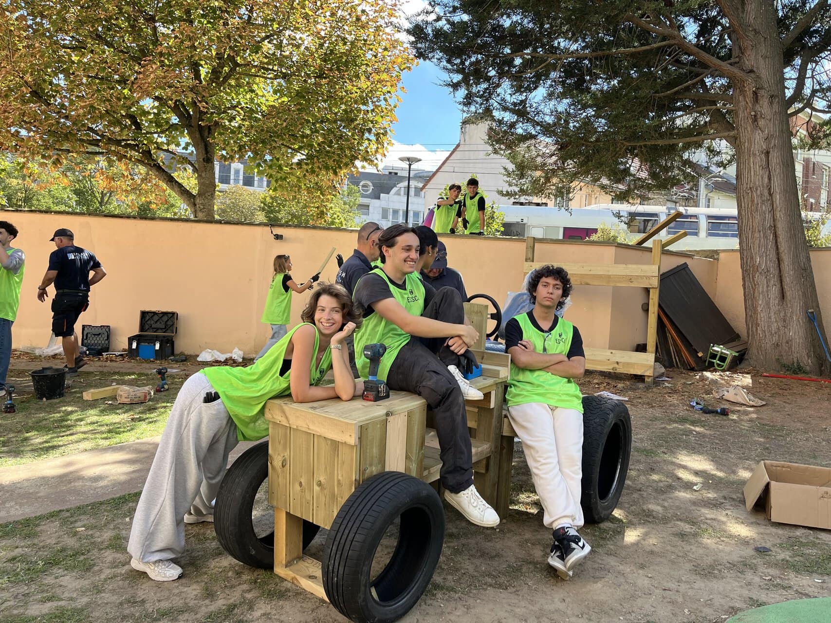 Jeunes bénévoles en gilets fluorescents construisant un chariot en bois sur chantier urbain.