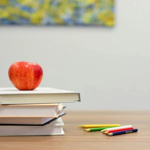 Pomme sur livres, crayons de couleur et blocs ABC sur table en bois, ambiance apprentissage.
