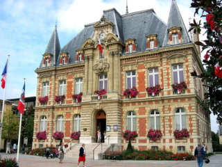 Mairie en brique et pierre, façade fleurie, toiture mansardée, drapeaux tricolores.