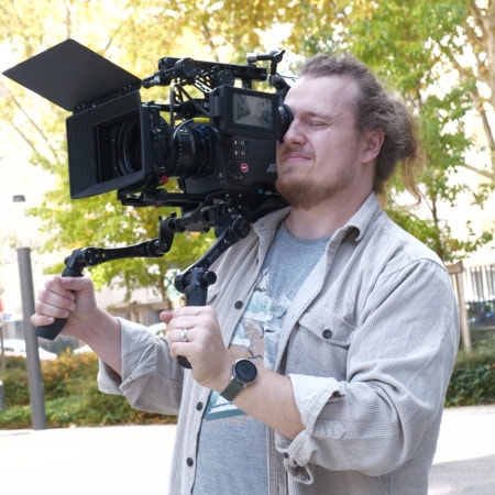 Opérateur caméra épaule professionnel en tournage extérieur, caméra cinéma avec matte box et moniteur.