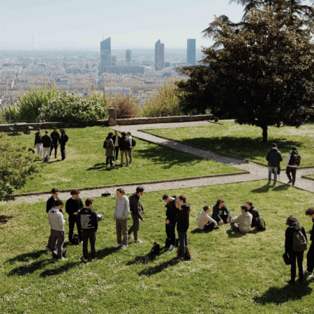 Étudiants sur pelouse urbaine surplombant ville, groupes, toits rouges et gratte-ciel.