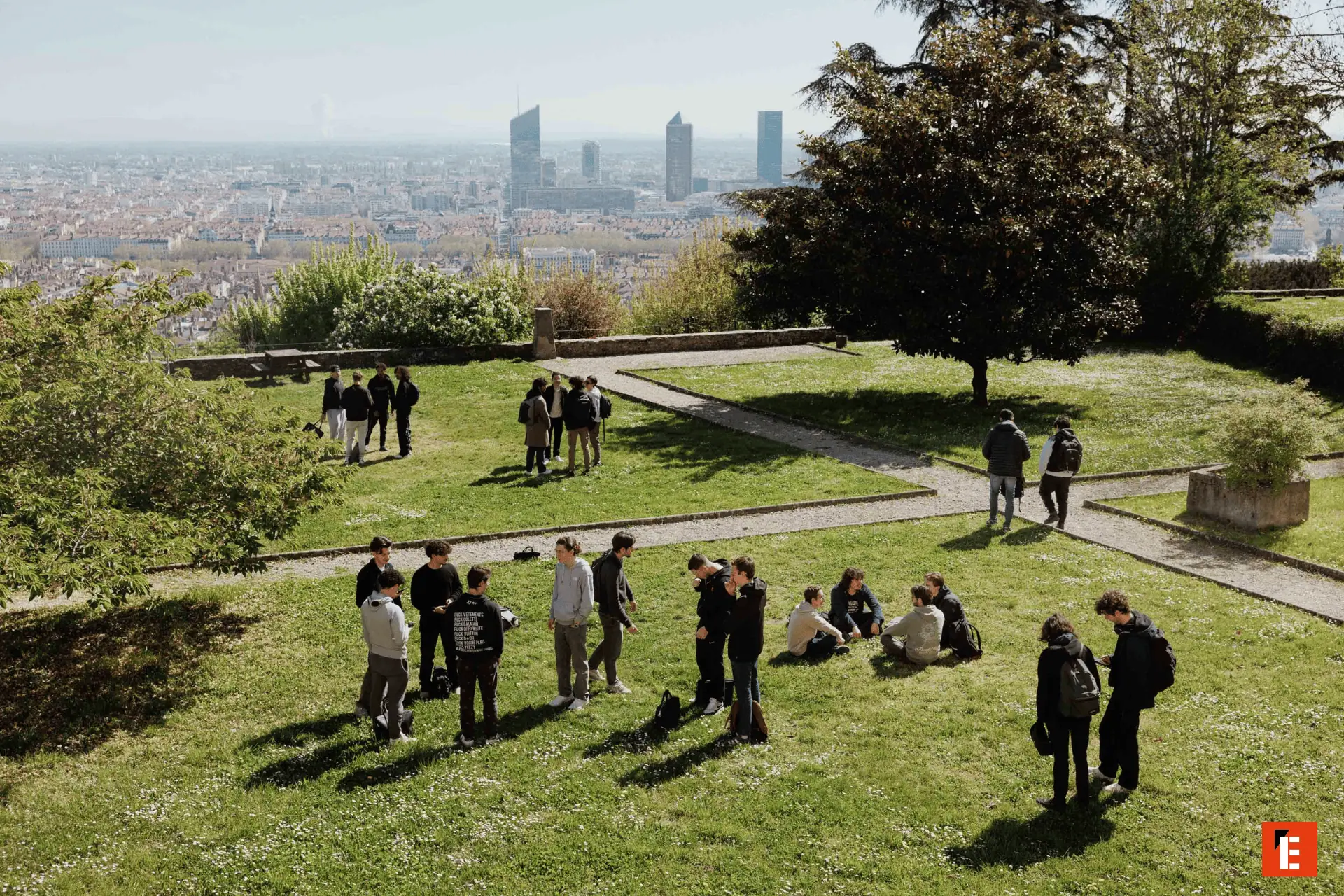 Étudiants sur pelouse urbaine surplombant ville, groupes, toits rouges et gratte-ciel.
