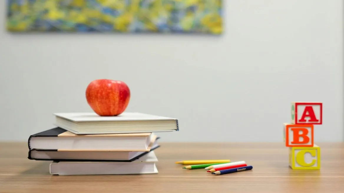 Pomme sur livres, crayons de couleur et blocs ABC sur table en bois, ambiance apprentissage.