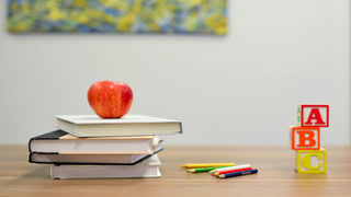 Pomme sur livres, crayons de couleur et blocs ABC sur table en bois, ambiance apprentissage.