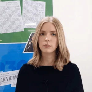 Portrait sérieux de jeune adulte blond avec micro, interview devant panneau dinformation institutionnel.