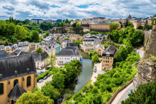 Quartier rive historique avec rivière sinueuse, maisons pastel, toits dardoise, falaises et église.