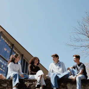 Quatre étudiants assis sur un mur de campus, discutant sous un ciel bleu printanier.