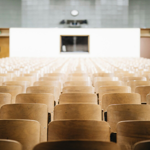 Salle de cours universitaire vide, rangées de chaises en bois alignées.