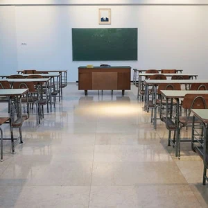 Salle de classe vide avec rangées de pupitres, tableau noir et bureau du professeur.