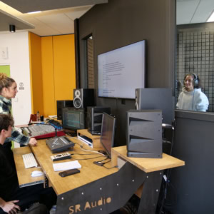 Studio denregistrement : régie avec console, moniteurs, ingénieur du son et vocaliste en cabine.