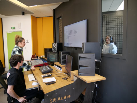 Studio denregistrement : régie avec console, moniteurs, ingénieur du son et vocaliste en cabine.