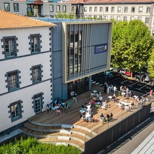 Terrasse bois animée du campus Clermont École de commerce, bâtiment ancien et annexe moderne.