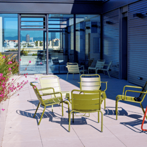 Terrasse sur toit moderne avec mobilier vert olive, tabourets rouges, plantes et vue urbaine.
