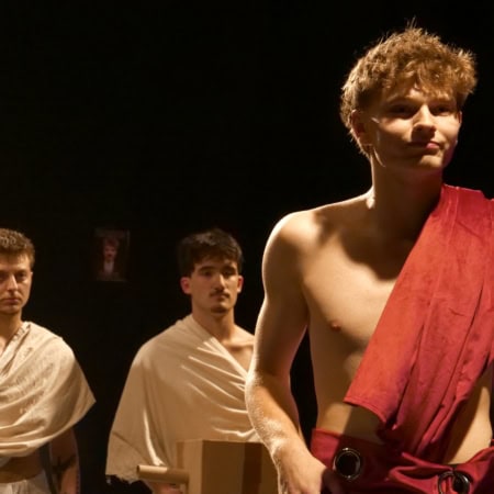 Trois hommes en toges sur scène théâtrale, éclairage dramatique et tableau classique.