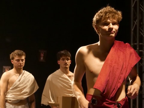 Trois hommes en toges sur scène théâtrale, éclairage dramatique et tableau classique.