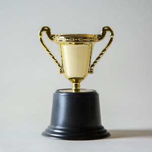 Petit trophée en or, coupe sur socle noir, fond neutre.