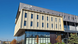 Bâtiment contemporain ESTP en verre et métal, façade surplombante, fenêtres verticales, ciel bleu.