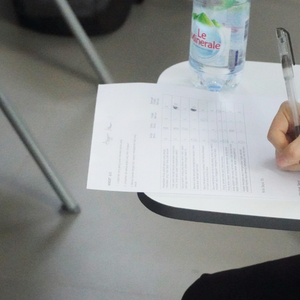 Élève écrit sur bulletin avec stylo sur tablette-bureau en salle de classe.