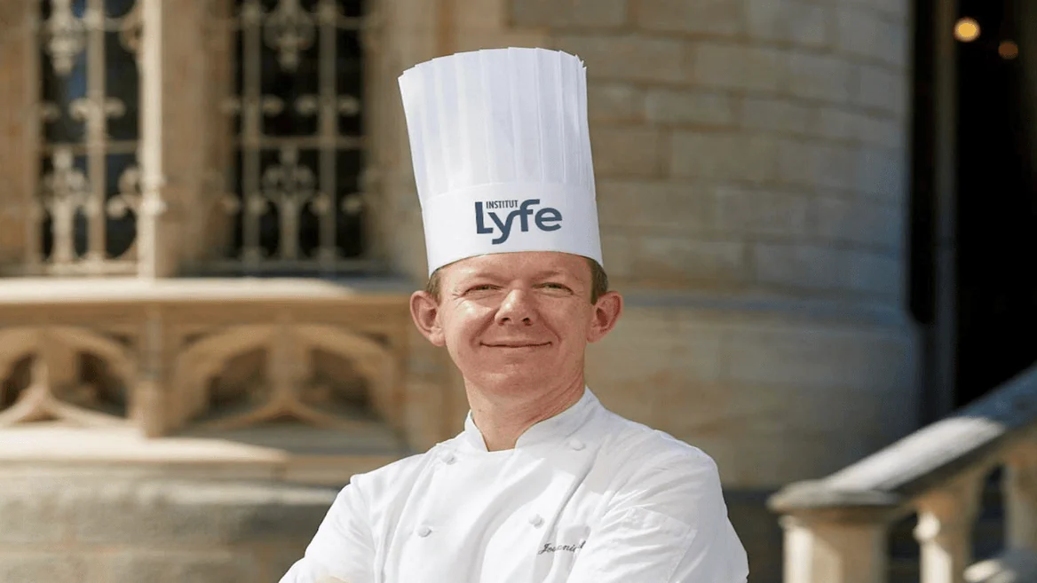 Chef professionnel en extérieur, portrait institut avec toque Lyfe et veste blanche.