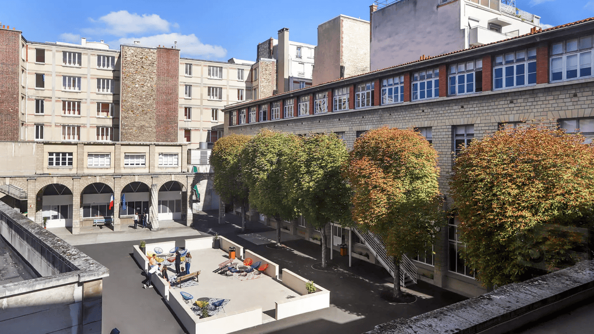Cour urbaine ensoleillée entourée de façades modernes, arbres, terrasse et chaises colorées.
